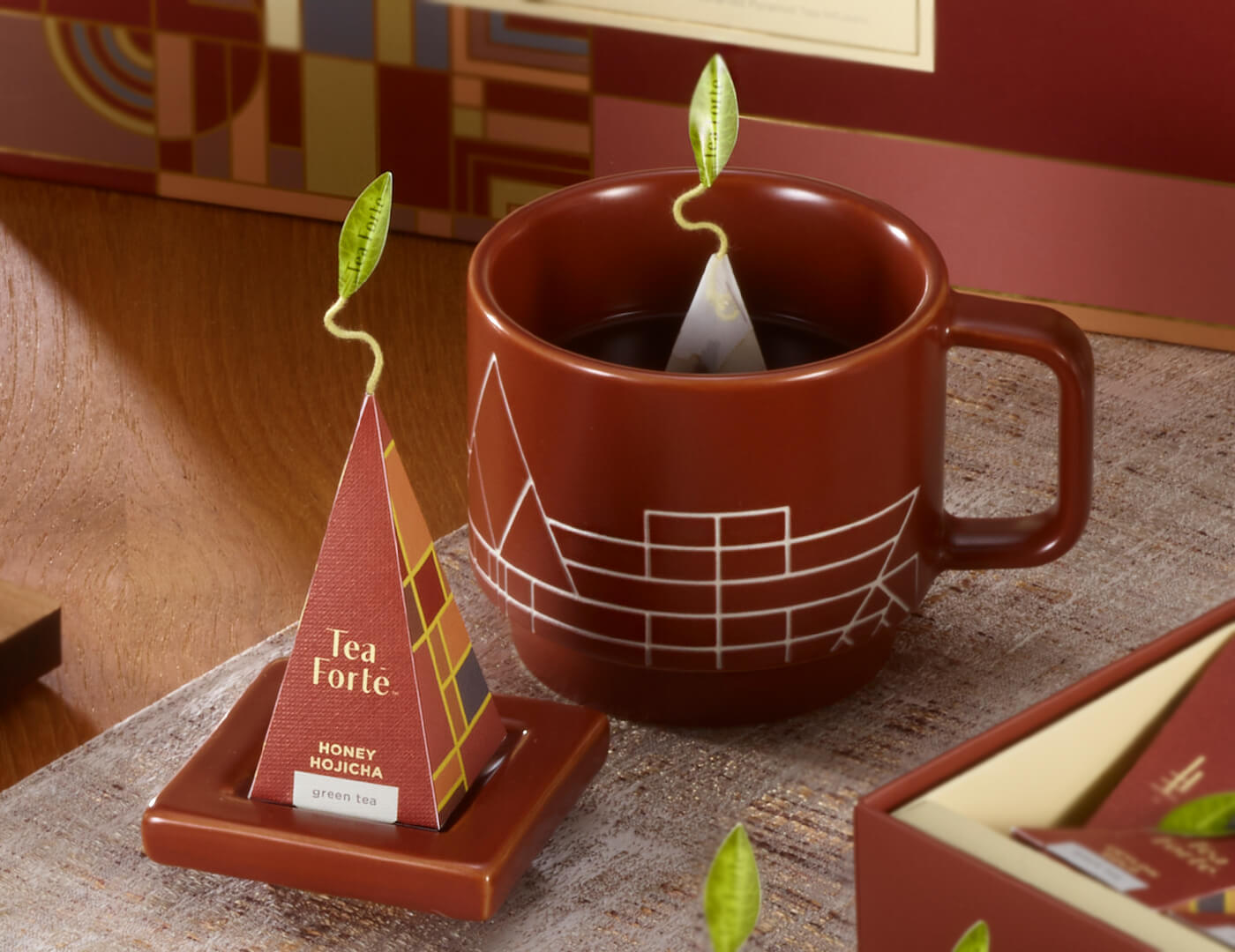 Frank Lloyd Wright teacup with infuser in Terra brown on wooden table with other Frank Lloyd Wright items