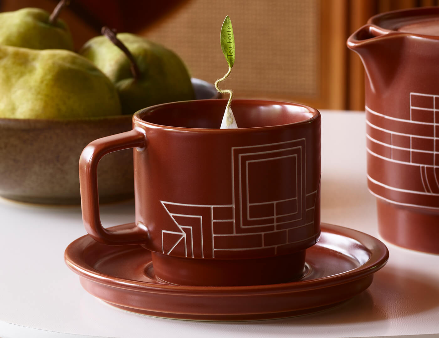 Terra stoneware teacup and saucer with a pyramid infuser inside on a table with pears